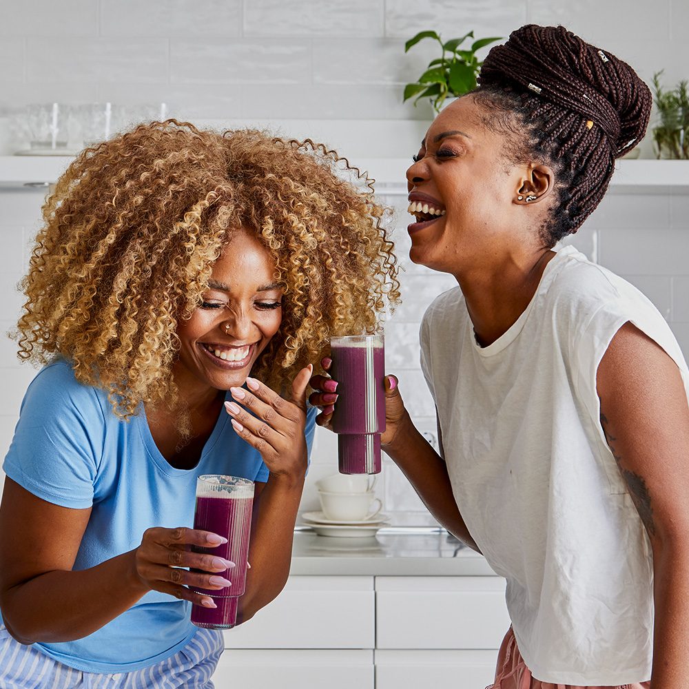 Two women laughing with berry smoothies in hand.